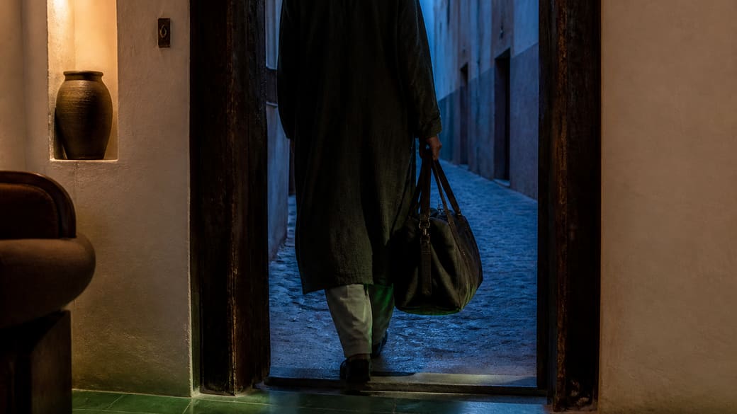 Voyageur non identifiable quittant un intérieur chaud à l'heure bleue, accompagné d'un reflet vert au seuil.